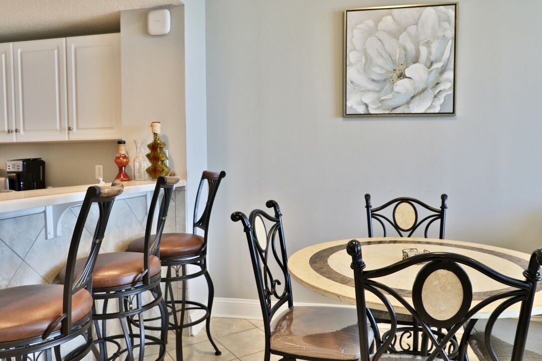 Un comedor con una mesa redonda y cuatro sillas, una cocina con armarios blancos y una obra de arte floral grande en la pared.