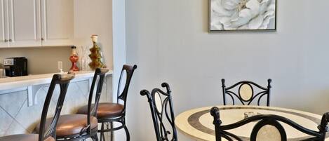 Un comedor con una mesa redonda y cuatro sillas, una cocina con armarios blancos y una obra de arte floral grande en la pared.