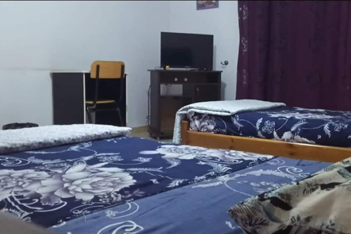 A bedroom with two beds, a TV on a stand, a chair, and a wardrobe.