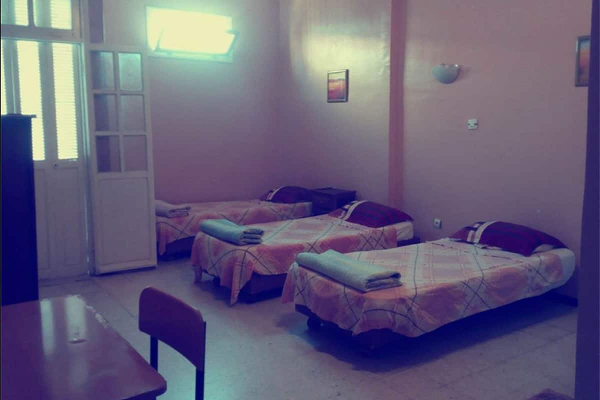 A room with three single beds, a table, and a chair.