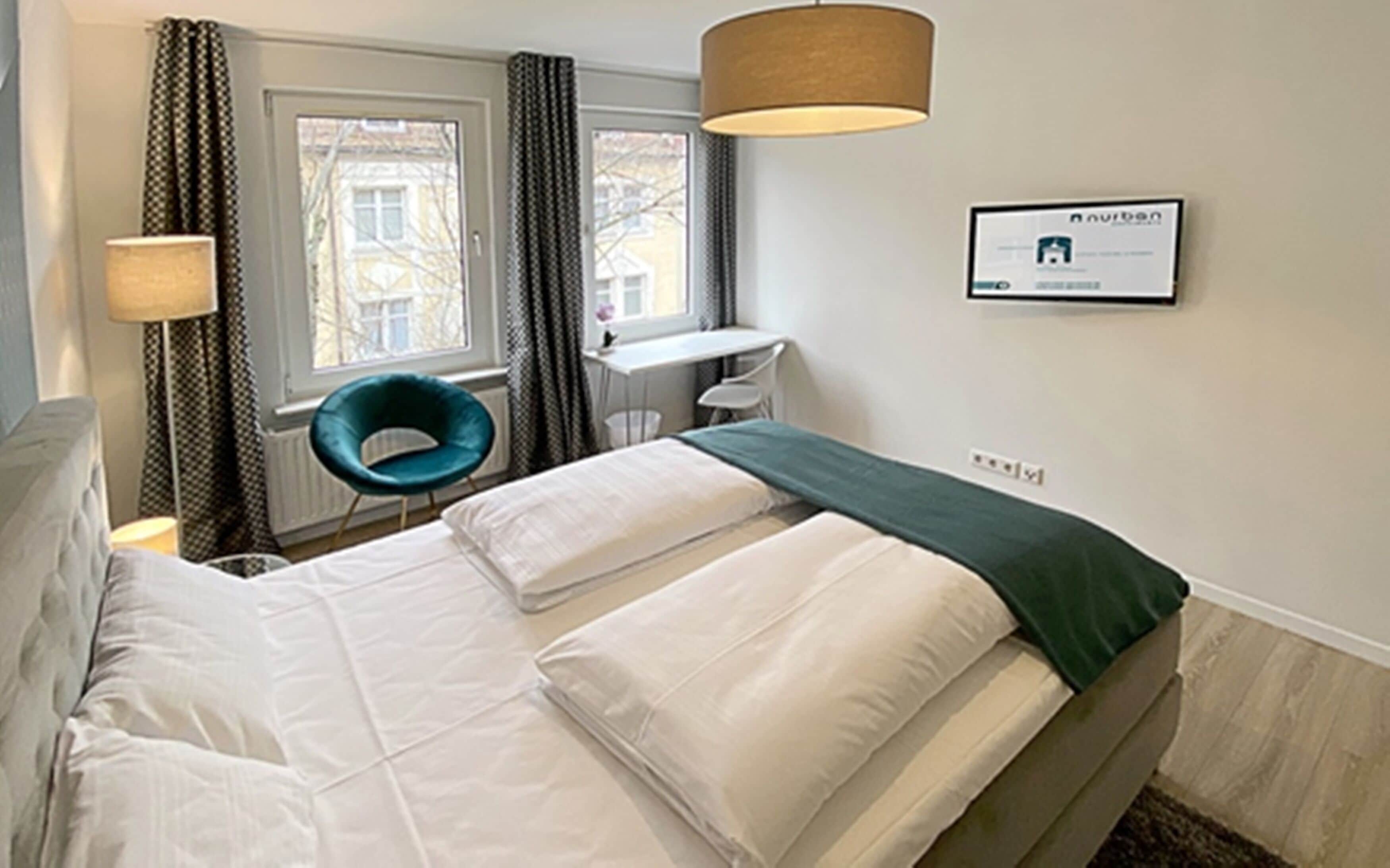 Ein Hotelzimmer mit Bett, Schreibtisch, Stuhl und einem fensterbepflanzten Fenster.