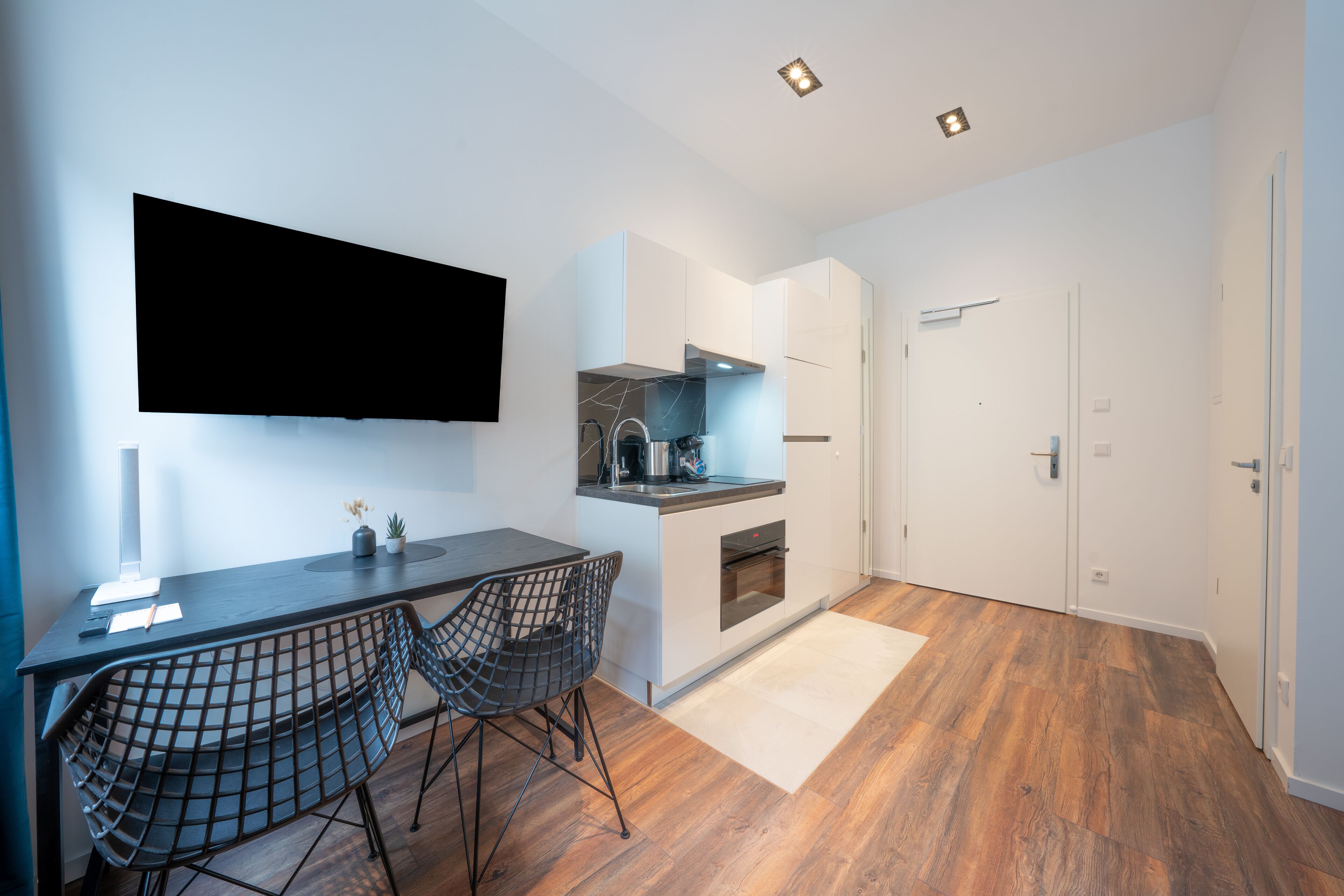 Une cuisine moderne dotée d’un téléviseur à écran plat, d’un coin repas avec une table et des chaises, et d’un plancher en bois.