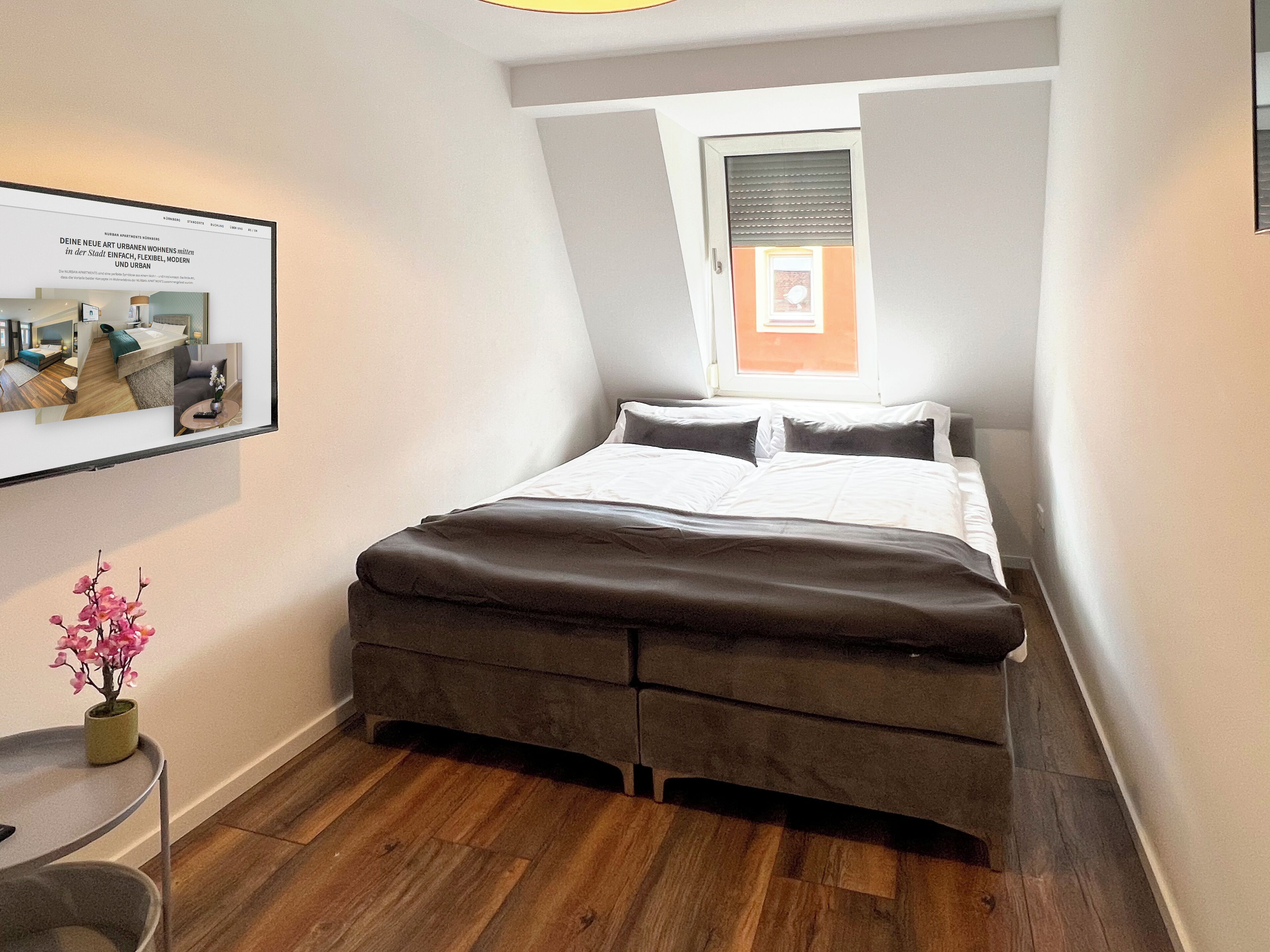 Un dormitorio con una cama, una mesita, una silla, una ventana con persianas y un cuadro en la pared.