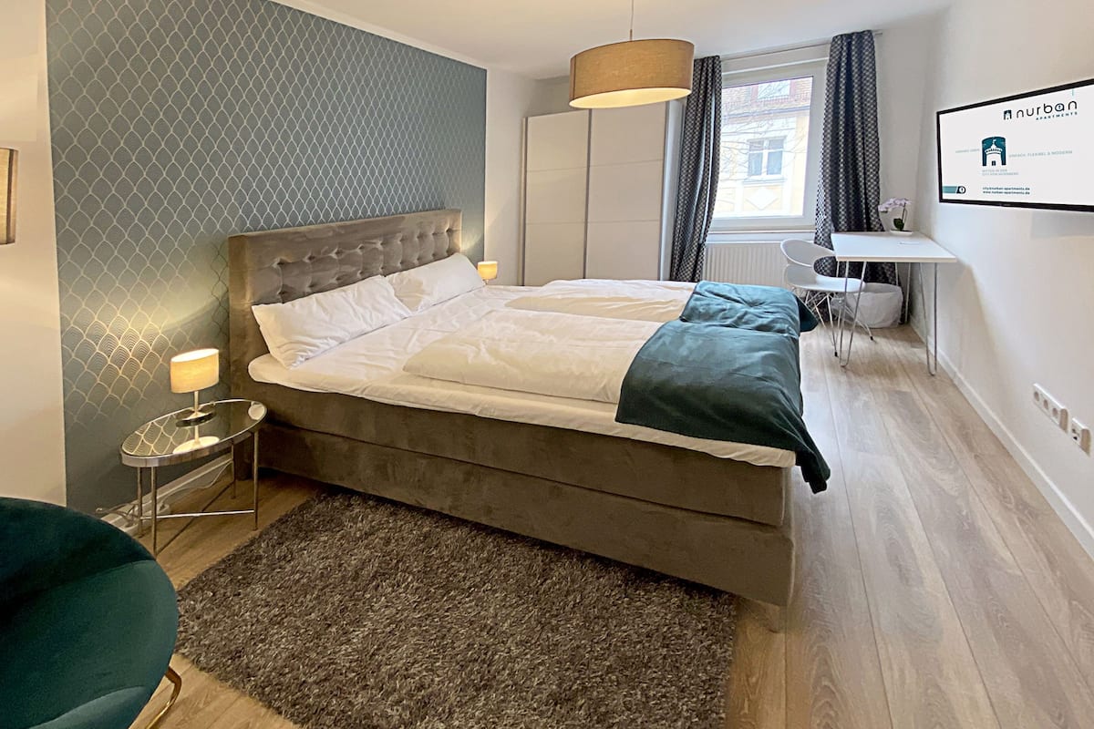 A modern bedroom with a large bed, a bedside table, a chair, and a desk.