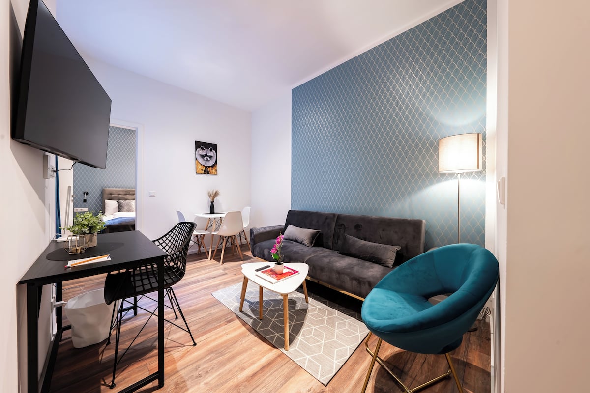 A modern living room with a sofa, a blue chair, a coffee table, and a TV mounted on the wall.