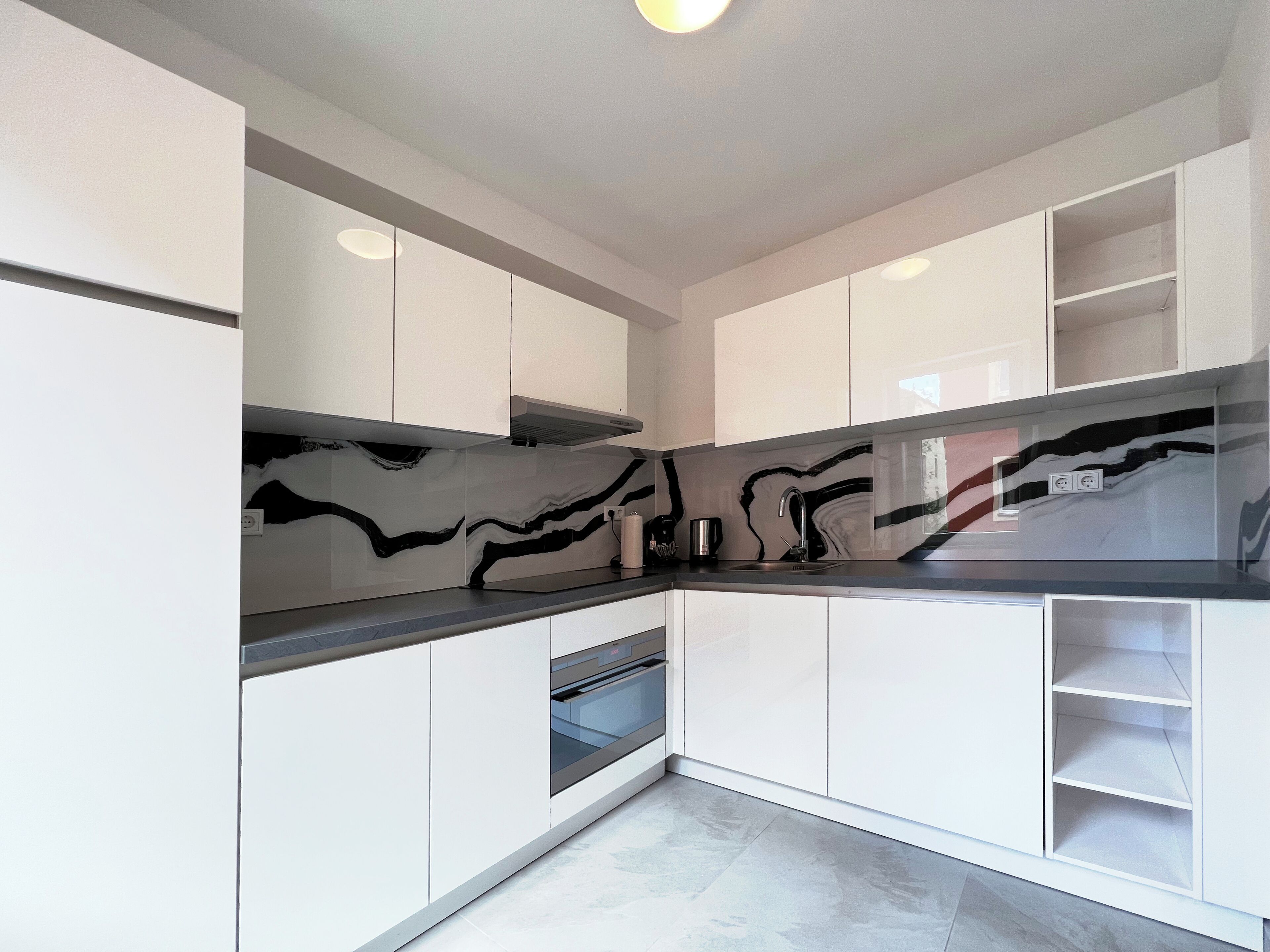 Una cocina moderna con armarios blancos, un salpicadero blanco y negro y un horno empotrado.