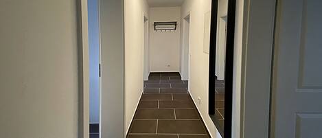 A hallway with dark tiled flooring, white walls, and a door on the right.
