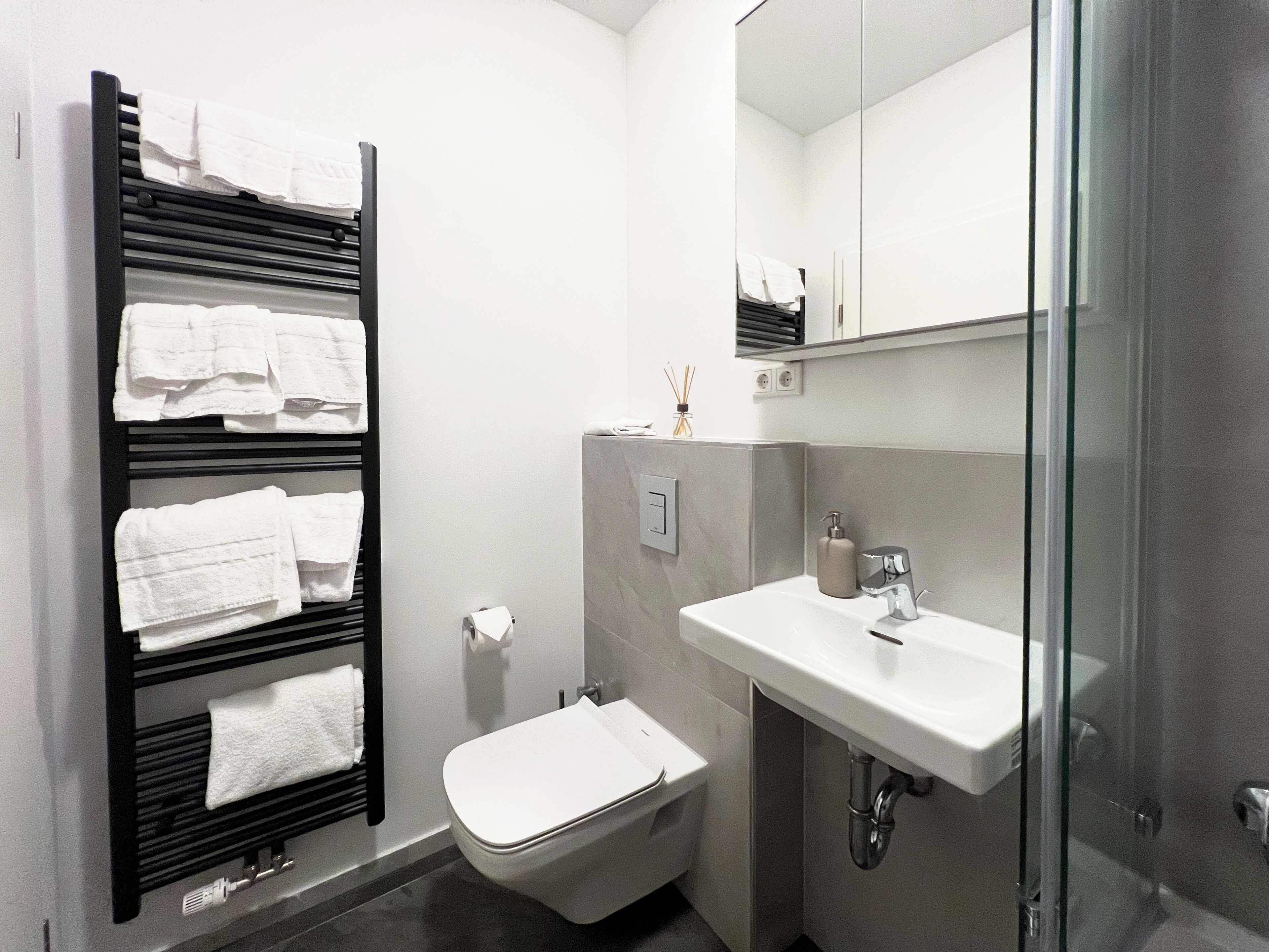 Un baño moderno con toallero negro, inodoro blanco y cabina de ducha de vidrio.