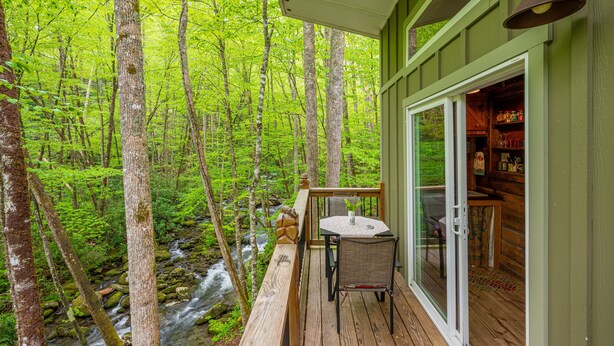 A wooden deck with a table and chairs overlooking a forest and a stream. - The Owl's Perch - Backwoods glamping cabin over amazing creek (Robbinsville)