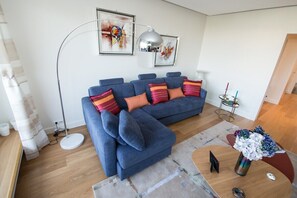 Ein modernes Wohnzimmer mit einem blauen Modulsofa, einer Stehlampe und abstrakter Kunst an der Wand.