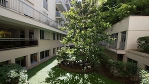 A courtyard with a central tree surrounded by greenery, modern buildings with balconies, and a well-maintained lawn. - Schloesing, 16e Tour Eiffel, Luxueux pied à terre (Paris)