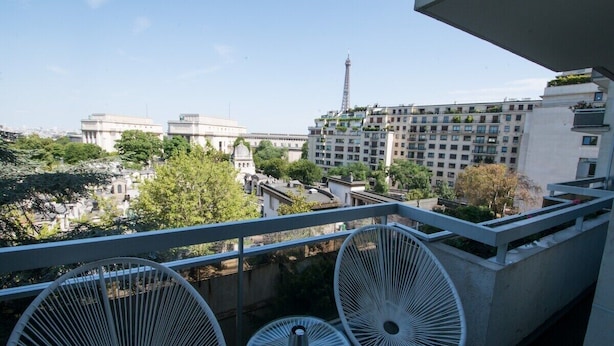 A balcony with white chairs and a view of a cityscape including a tall tower. - Schloesing, 16e Tour Eiffel, Luxueux pied à terre (Paris)