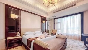 A hotel room with a large bed, a bedside table, a mirror, a chair, and a large window with curtains. - Rendezvous Hotel (CHANGZHI)
