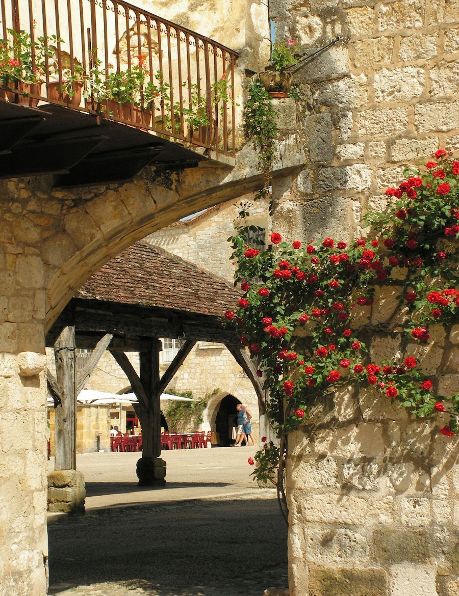 An outdoor courtyard with stone walls, a wooden pergola, and red roses.
