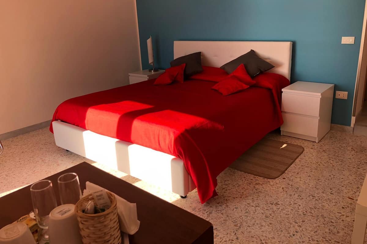 A bedroom with a red bedspread, white nightstands, and a blue wall.