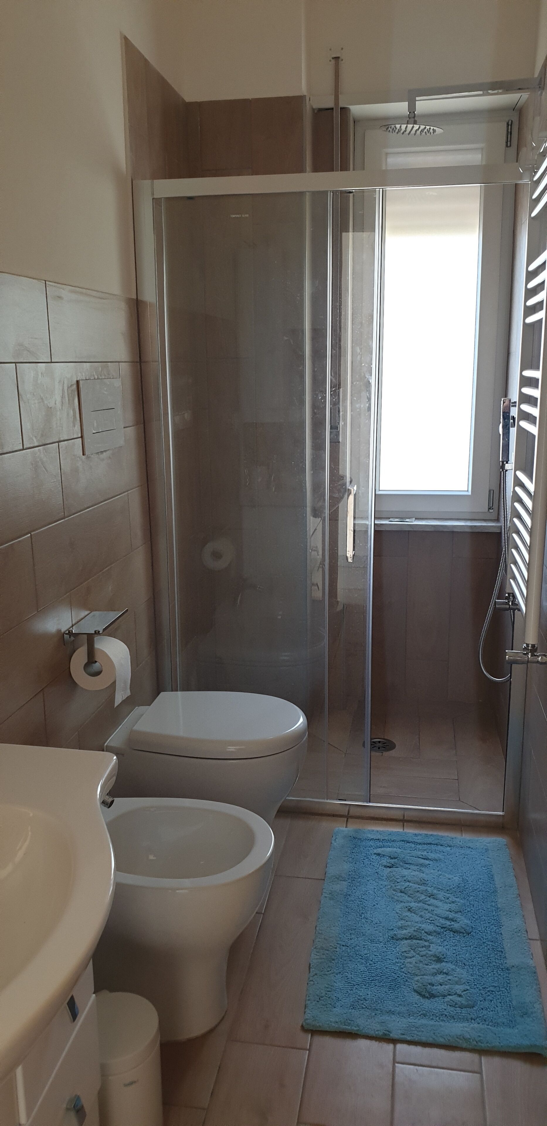 Un baño con inodoro, bidé y zona de ducha con mampara de vidrio.