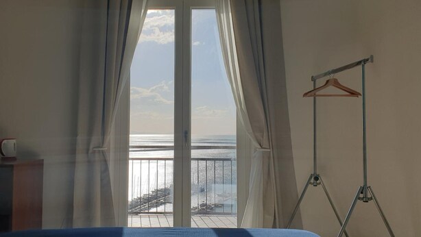 Ein Zimmer mit einem Bett, einem Holzschrank, einer Kleiderstange und Meerblick durch ein großes Fenster.