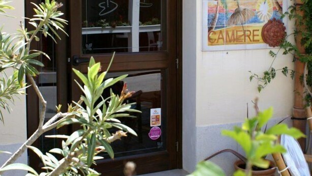 A storefront with a sign reading "LA CARIBENA" and a mural depicting palm trees and a beach scene. - La Caribena (San Vito Lo Capo)