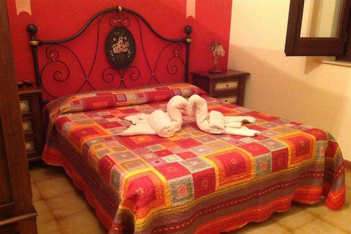 Un lit recouvert d’une courtepointe aux couleurs vives, avec deux serviettes disposées en forme de cœur sur le lit.