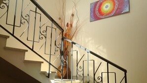 A staircase with a metal railing, a vase with dried plants, and a colorful abstract painting on the wall. - La Caribena (San Vito Lo Capo)