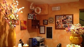 A reception area with a wooden desk, a printer, a coffee machine, and a vase with flowers. There are framed photos and a clock on the wall. - La Caribena (San Vito Lo Capo)