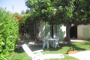 Un patio con mesa y sillas, rodeado de follaje y un árbol.
