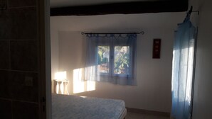 Quarto com cama, janela com cortinas, radiador e uma pequena mesa.