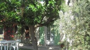 Um pátio com mesa e cadeiras, rodeado por vegetação e um edifício ao fundo.