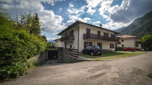 A two-story house with a garage, a red car parked in front, and a mountain in the background. - Residence Fiore (Ledro)