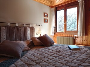 Ein Schlafzimmer mit einem Bett, einem Vorhangfenster, einem Heizkörper und einem kleinen Tisch mit einer Lampe.