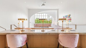 Een moderne keuken met een centraal eiland, twee roze stoelen en hanglampen.