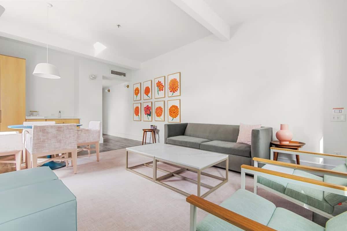 Una sala de estar moderna con un sofá, una mesa de centro y sillas. Hay una zona de cocina con una mesa de comedor y sillas.
