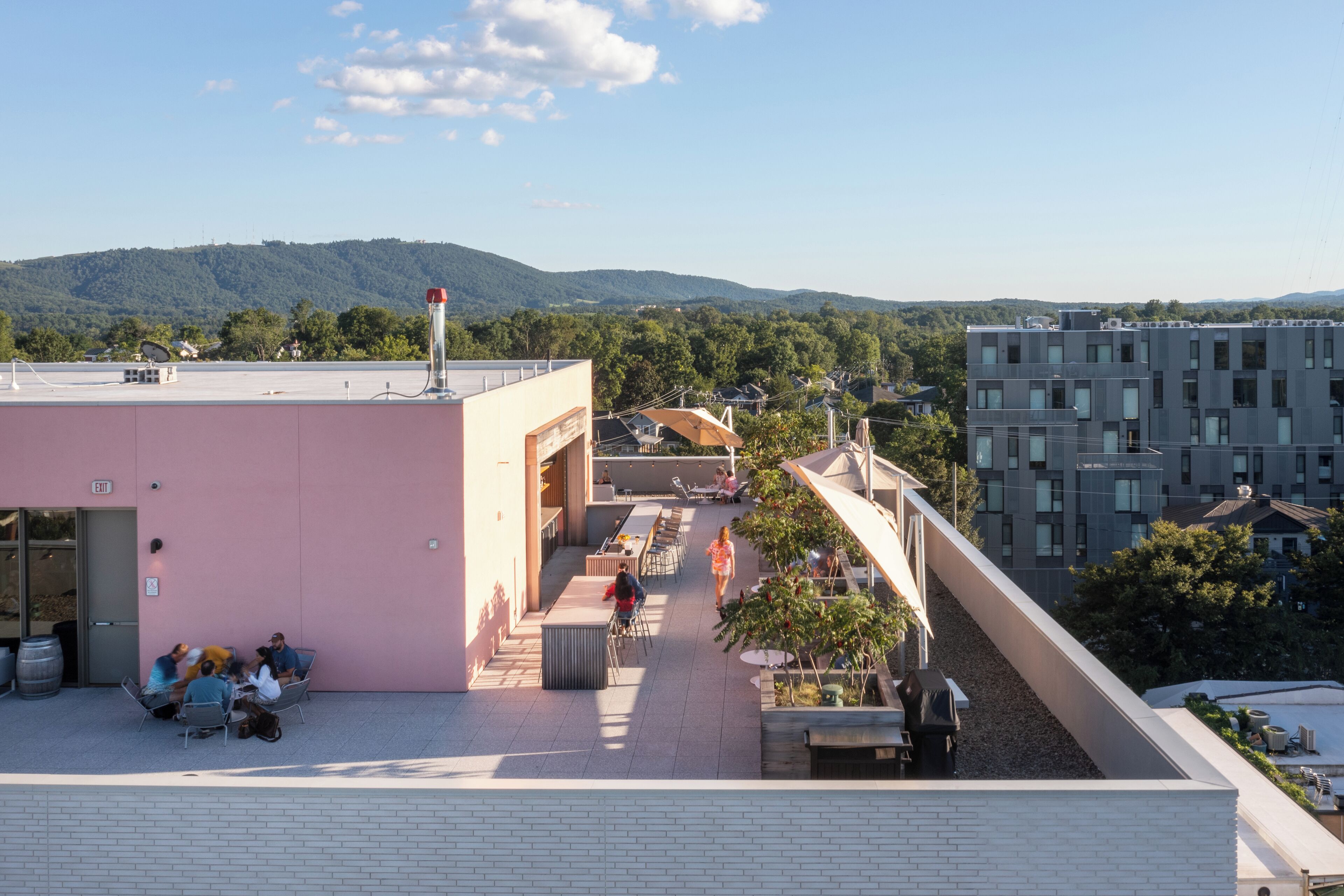 A rooftop terrace with outdoor seating, a pink building, and a view of distant hills.