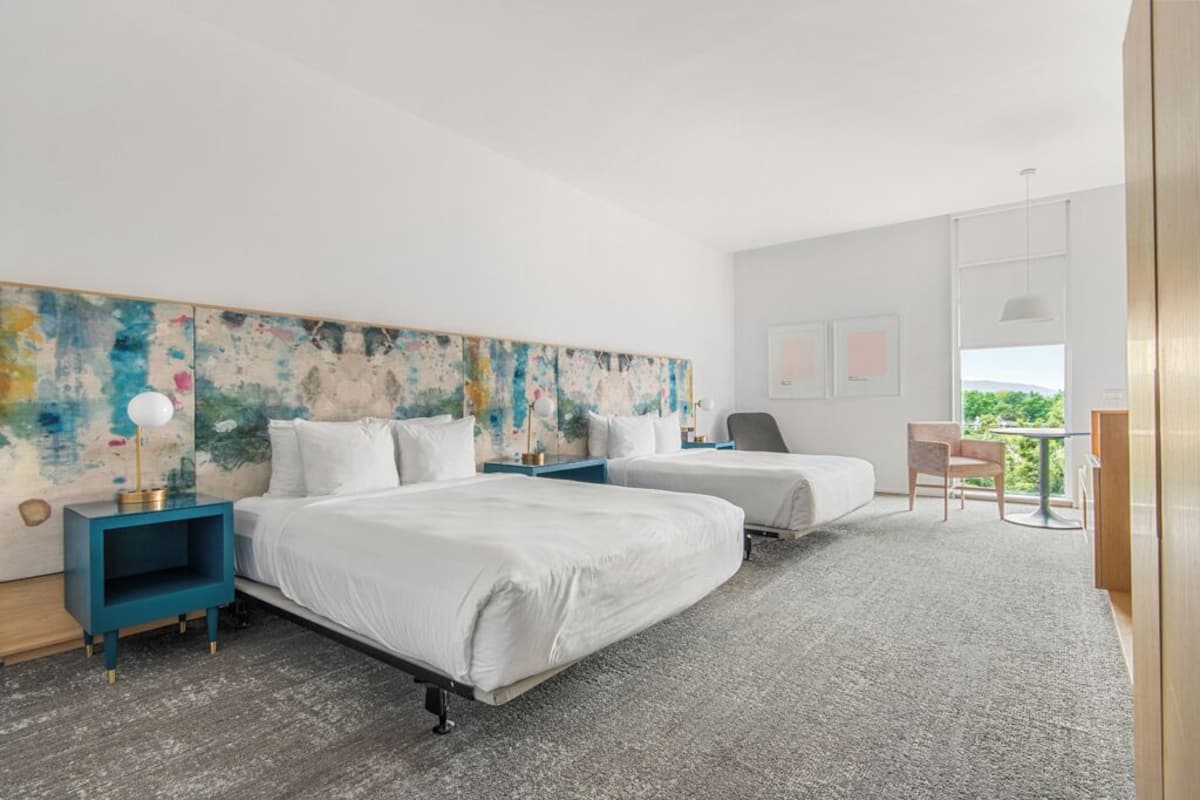 Habitación de hotel moderna con dos camas, un cuadro abstracto grande en la pared, un escritorio con una silla y vistas a zonas verdes por la ventana.
