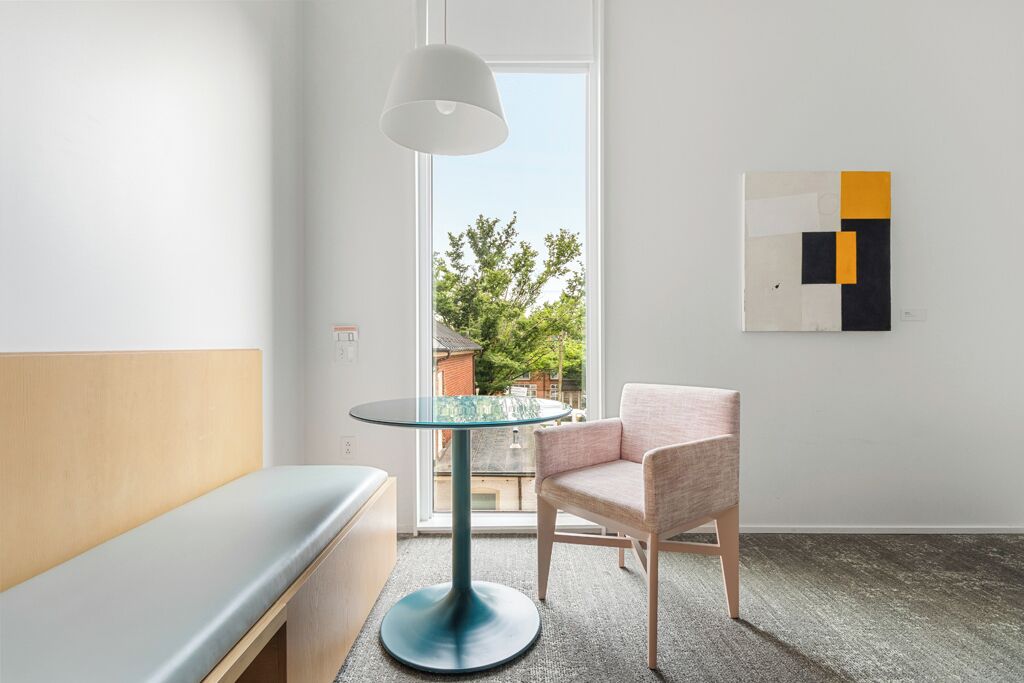 Habitació moderna amb taula rodona de vidre, una banca amb coixins, una cadira i una obra d'art abstracta penjada a la paret.