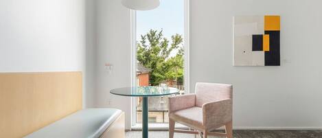 Habitació moderna amb taula rodona de vidre, una banca amb coixins, una cadira i una obra d'art abstracta penjada a la paret.