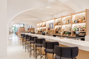 Un bar moderno con una barra alargada, varias estanterías llenas de botellas de licor y taburetes de bar.