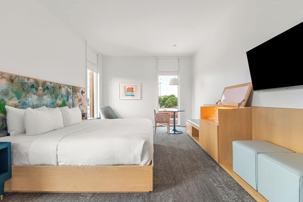 Habitación de hotel moderna con una cama grande, un escritorio, una silla, un televisor y un cuadro en la pared.