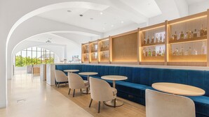 Een moderne barruimte met blauwe zitplaatsen, ronde tafels en een wand met verlichte flessen.