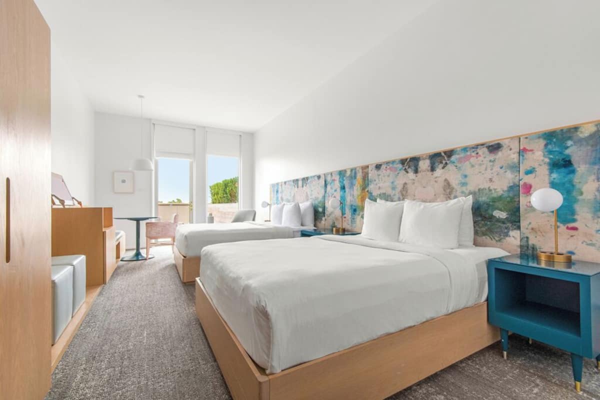 Una habitación de hotel moderna con dos camas, un escritorio y un cuadro abstracto grande en la pared.