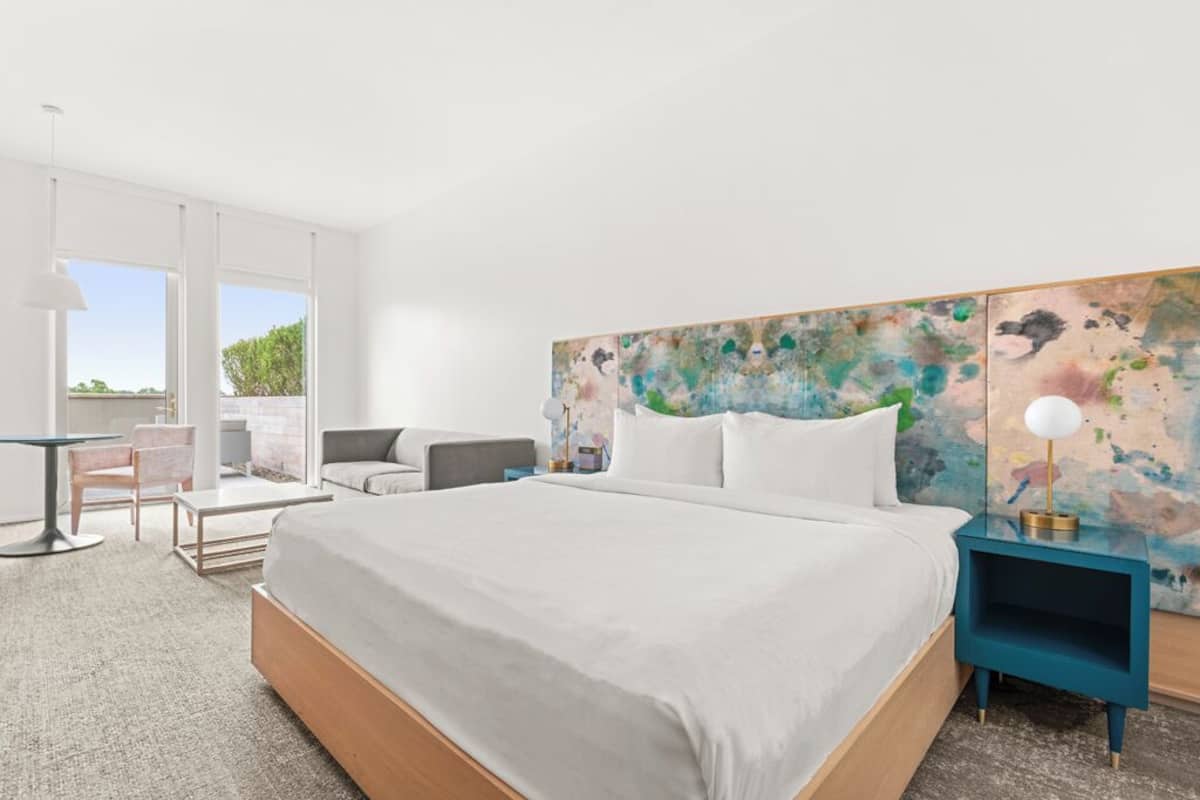 Un dormitorio moderno con una cama grande, un escritorio, una silla y un cuadro abstracto y colorido en la pared.