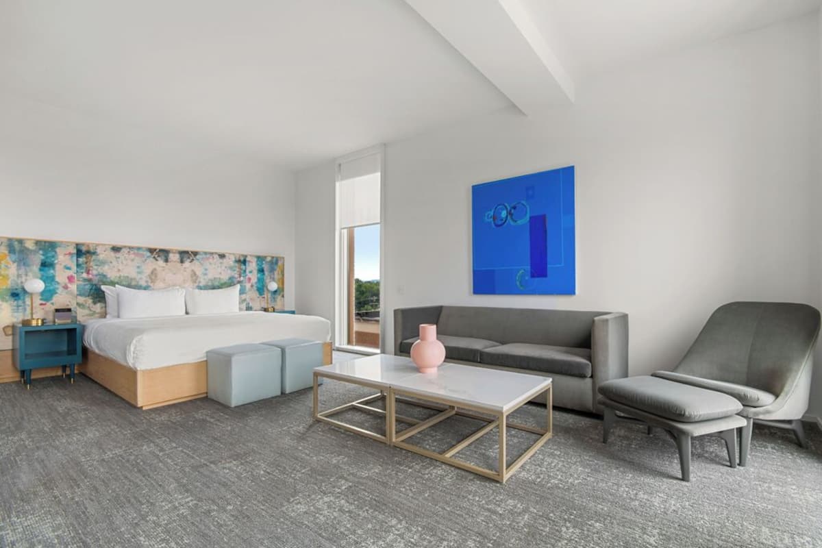 Una habitación de hotel moderna con cama, sofá, sillón y mesa de centro.