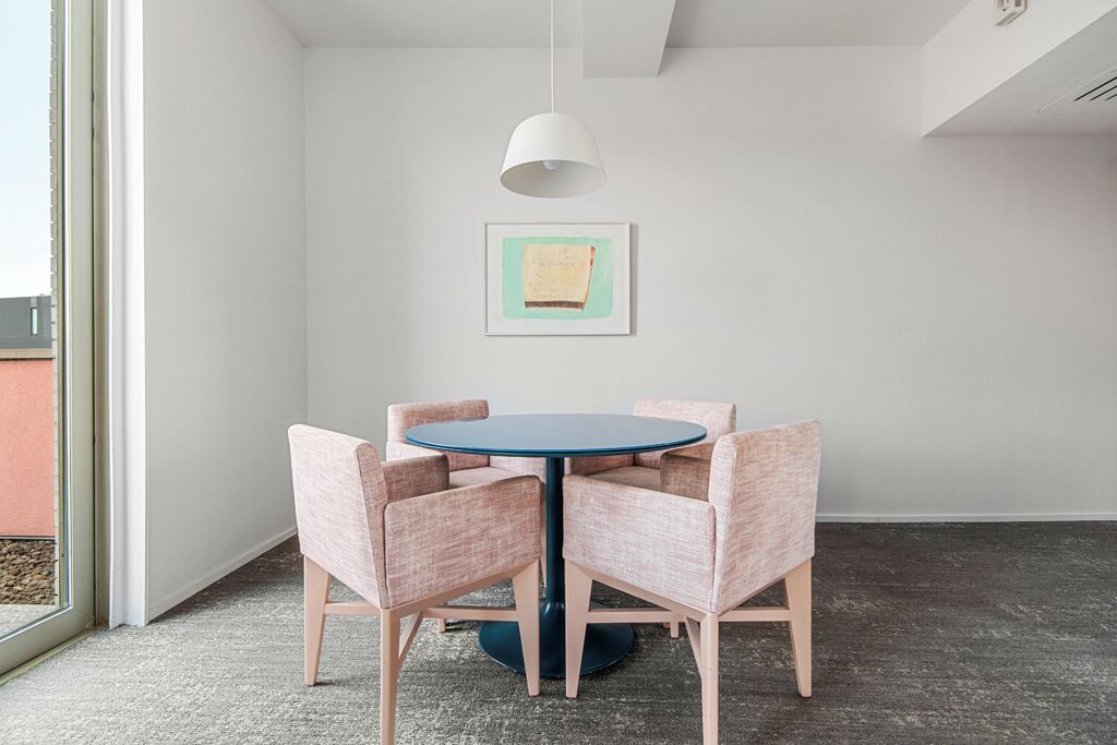 Ein Zimmer mit einem runden Tisch, vier Stühlen, einer Pendelleuchte und einem gerahmten Bild an der Wand.
