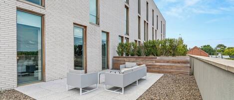 A modern building with a patio area featuring outdoor seating and a landscaped garden.