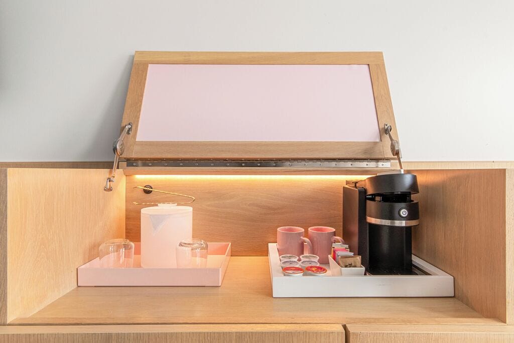 A wooden cabinet with a coffee maker, cups, and a tray.