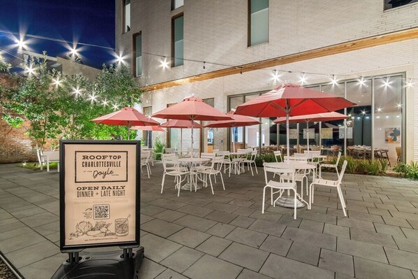 An outdoor patio with white tables and red umbrellas at Rooftop Charlotteville at the Doyle Hotel.