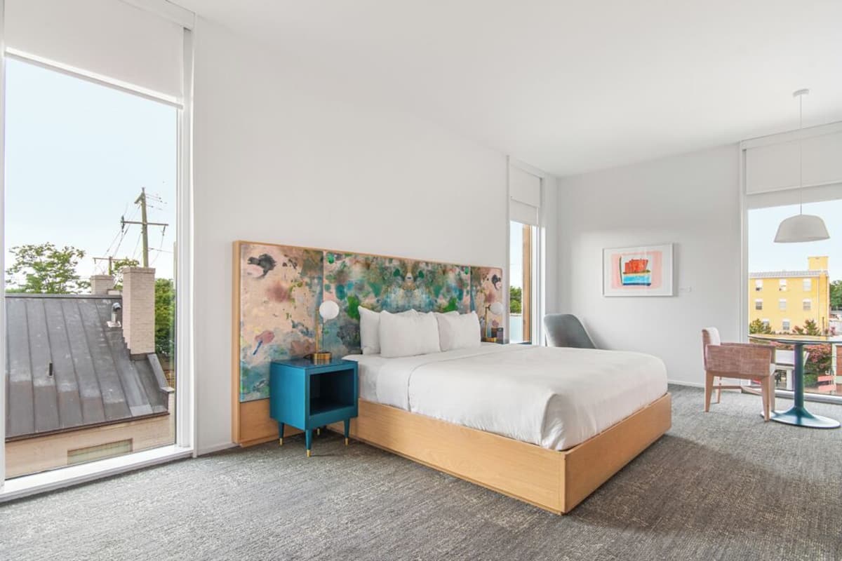 Una habitación de hotel moderna con una cama grande, una mesita de noche azul, una silla y una mesa.