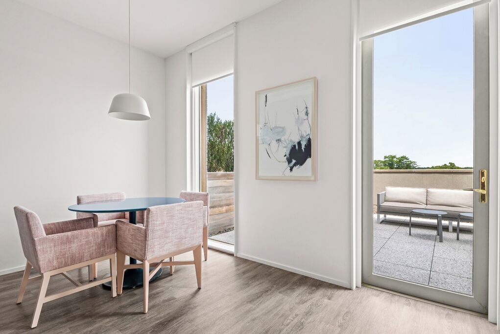 A modern dining area with a round table and chairs, a pendant light, and a sliding glass door leading to an outdoor seating area.