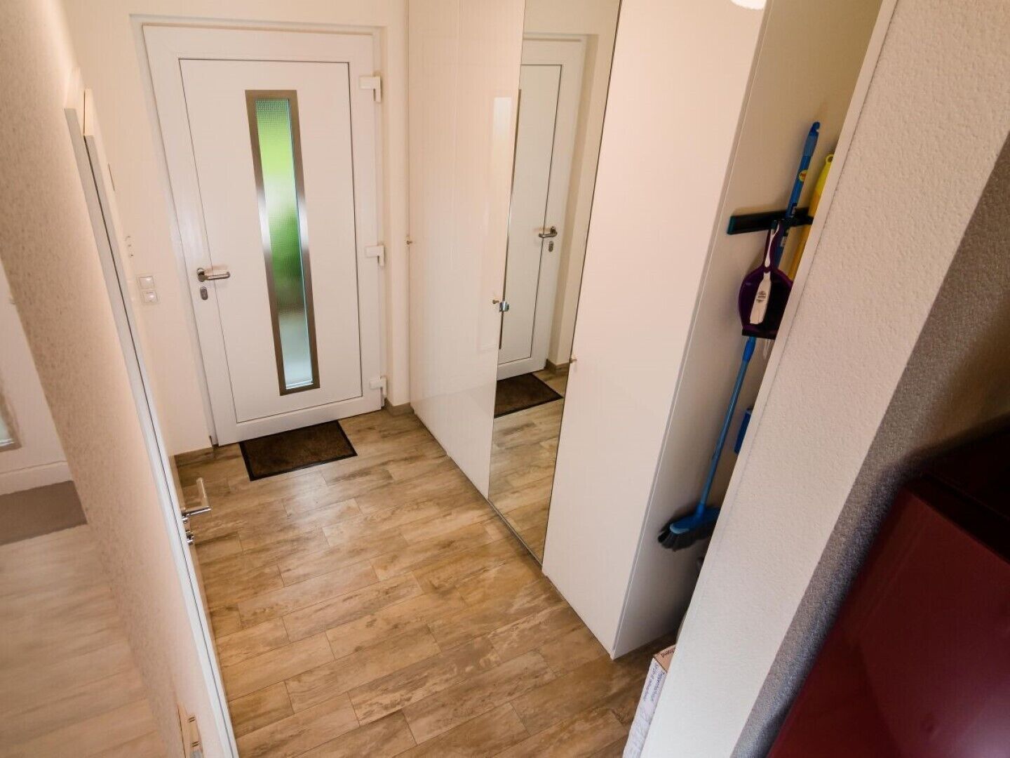 A hallway with wooden flooring, white walls, and a door with a frosted glass panel.