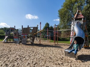 Ein Spielplatz mit Rutsche und Klettergerüsten auf Sandboden.